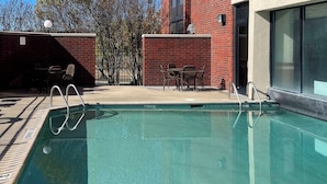 A swimming pool with a no diving sign, surrounded by a brick wall, a table with chairs, and a building with large windows. - Prado Hotel (Ridgeland)