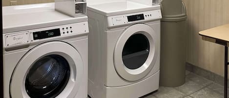 A laundry room with two front-loading Whirlpool washers and a trash can.