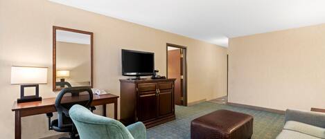 Ein Hotelzimmer mit Schreibtisch, Fernseher, Sessel, Sofa und Schrank.