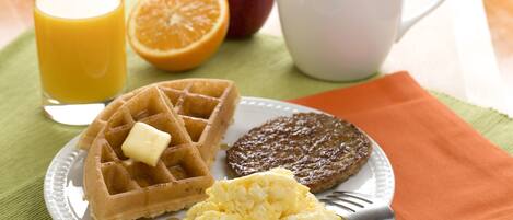 A plate with waffles, scrambled eggs, and a patty, accompanied by a glass of orange juice and a cup of coffee.