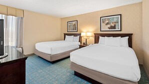 A hotel room with two beds, a desk, a TV, and two framed pictures on the wall. - Prado Hotel (Ridgeland)