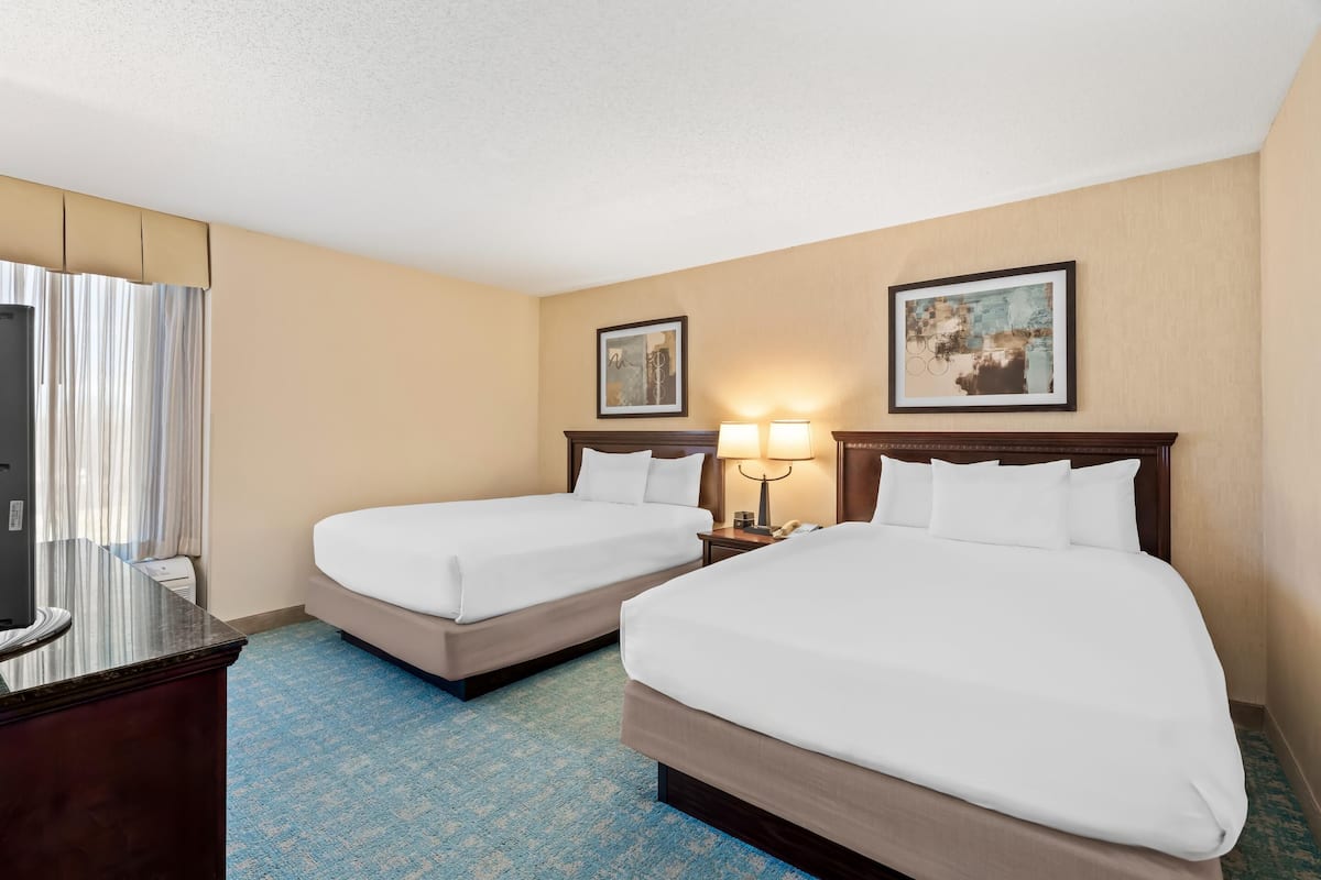 A hotel room with two beds, a desk, a TV, and two framed pictures on the wall.