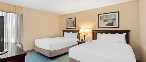 A hotel room with two beds, a desk, a TV, and two framed pictures on the wall.