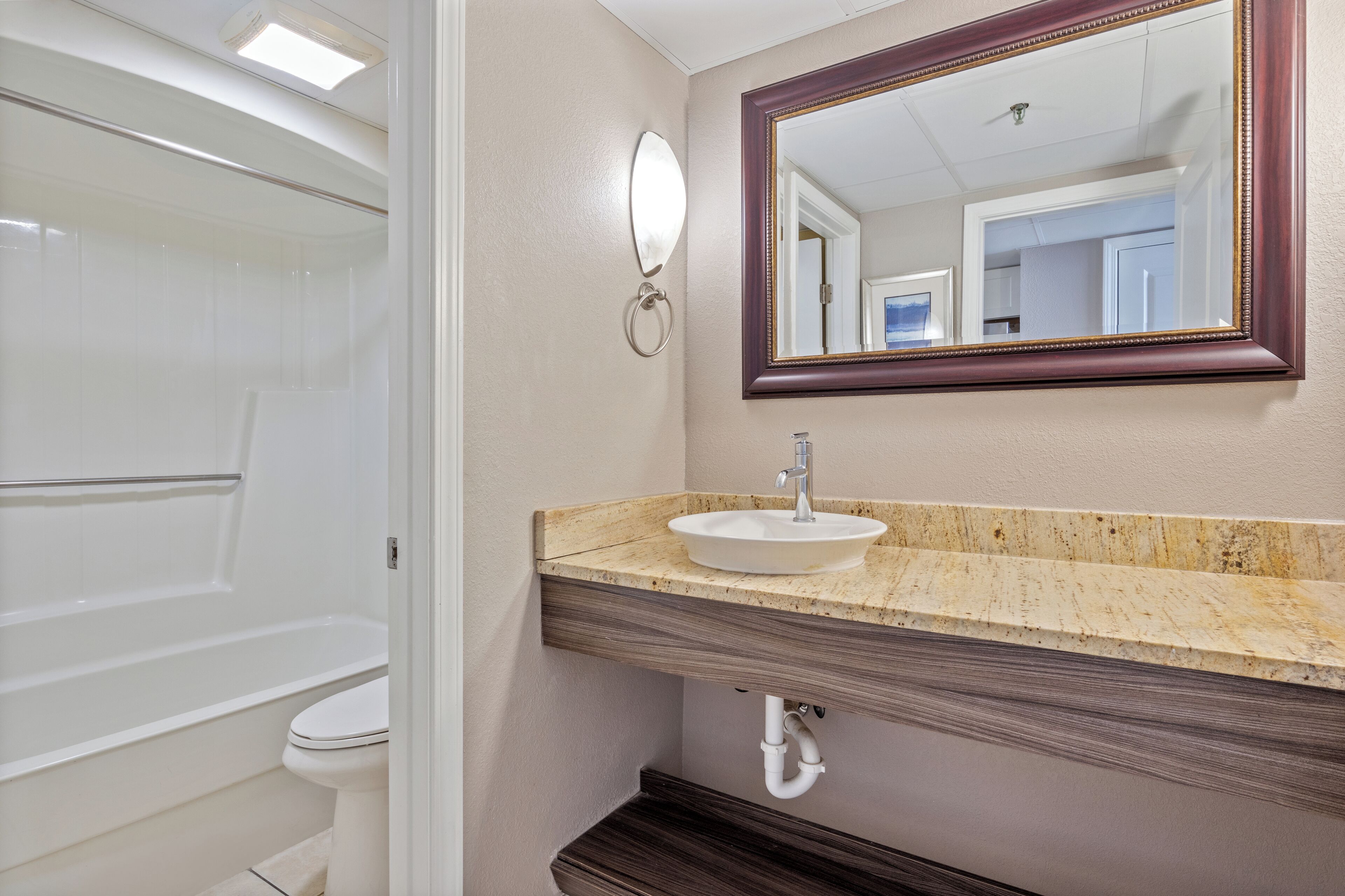 A bathroom with a white bathtub, a white toilet, a beige vanity with a marble countertop, and a large mirror with a wooden frame.