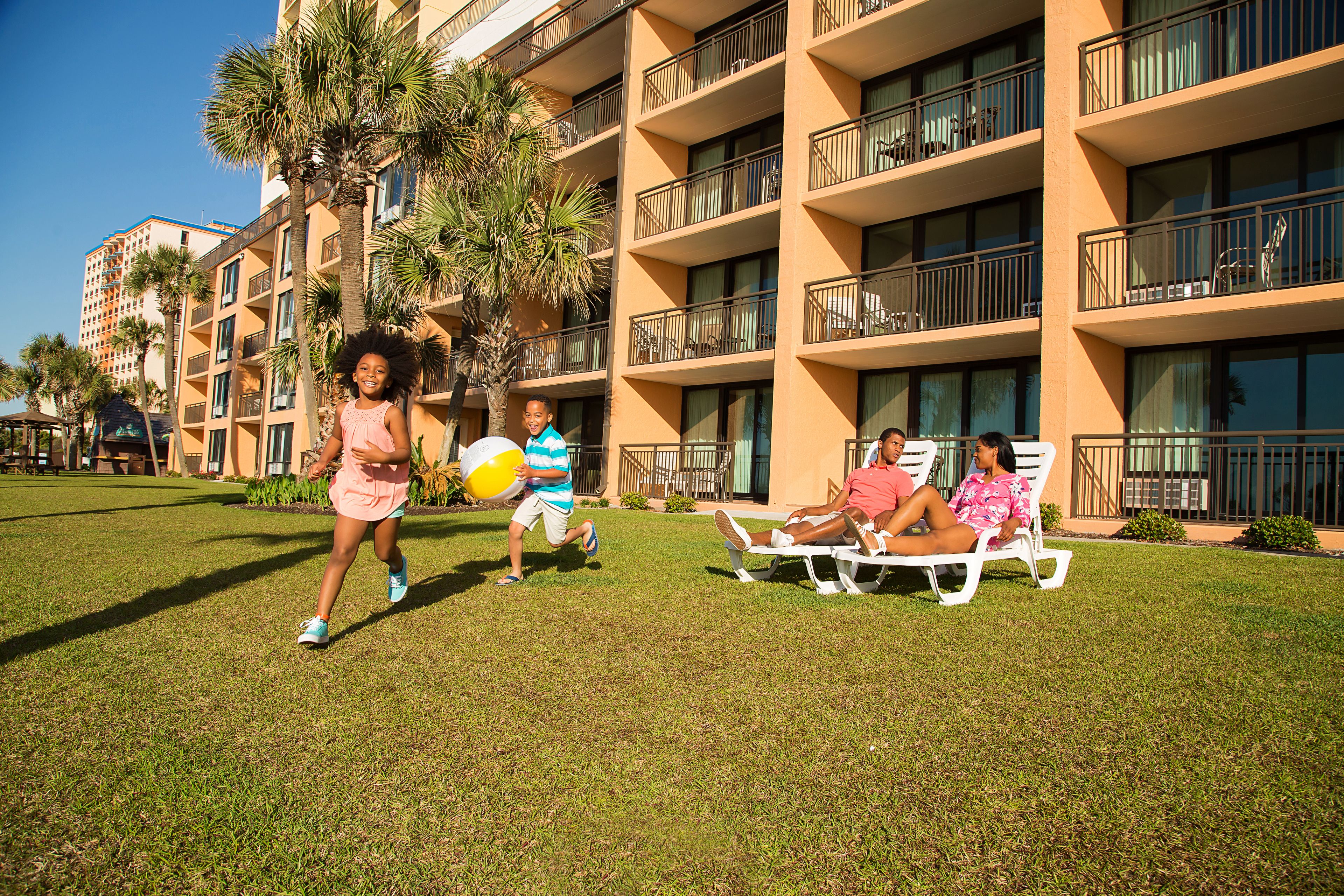 A hotel courtyard with a grassy lawn, palm trees, and a building with balconies.