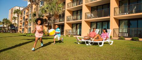 A hotel courtyard with a grassy lawn, palm trees, and a building with balconies.