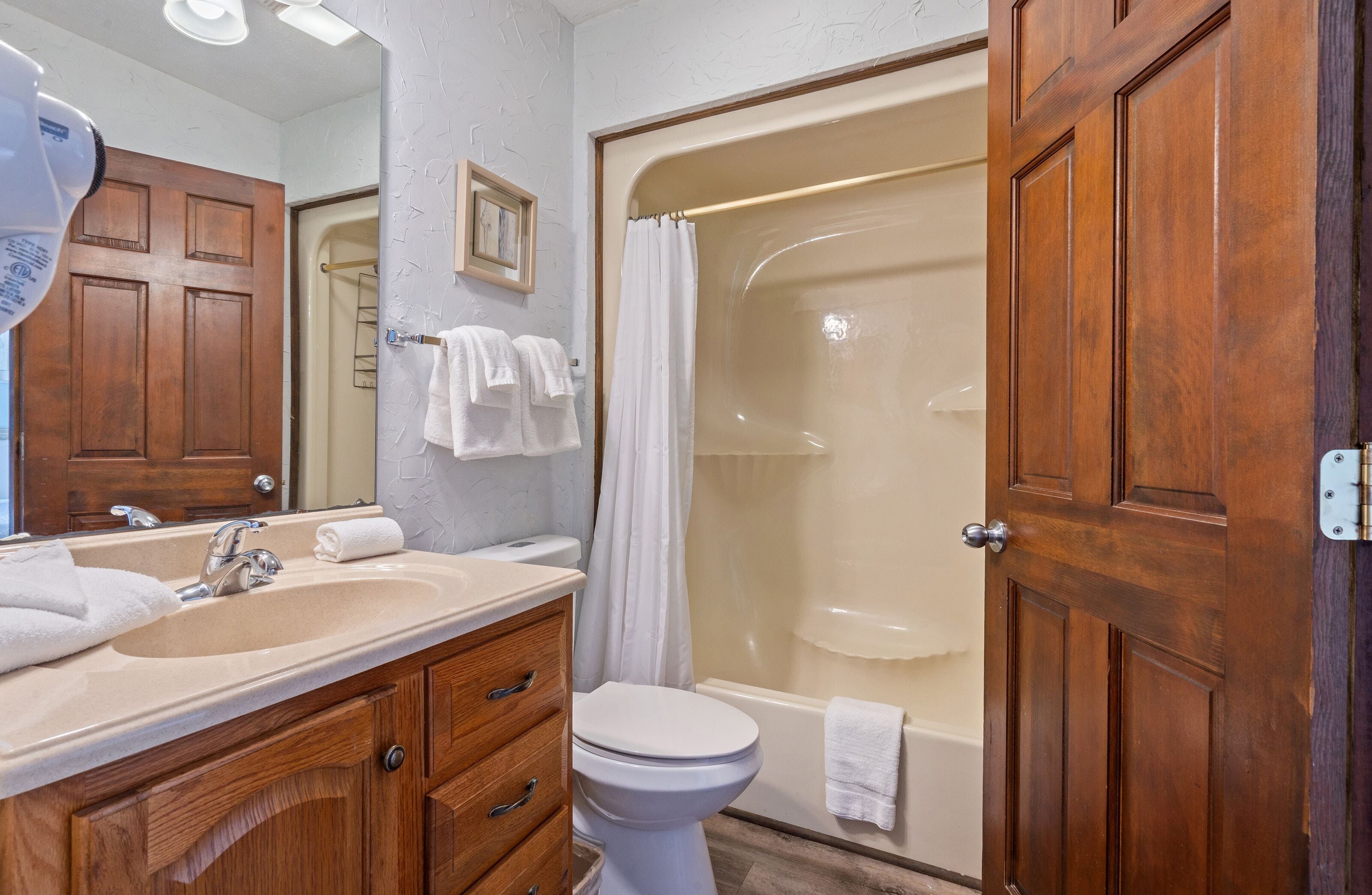Un bagno con un mobile lavabo in legno, un lavandino, un WC, una doccia e una porta.
