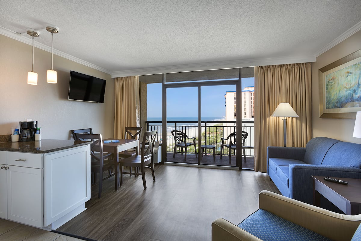 Una habitación de hotel con balcón, zona de comedor, sofá y televisión.
