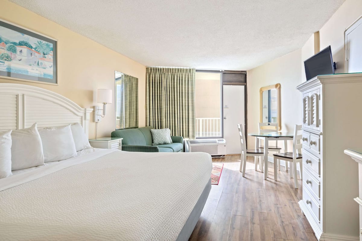 Habitación de hotel con una cama grande, un sofá verde, un escritorio con una silla, un aparador y un televisor encima.
