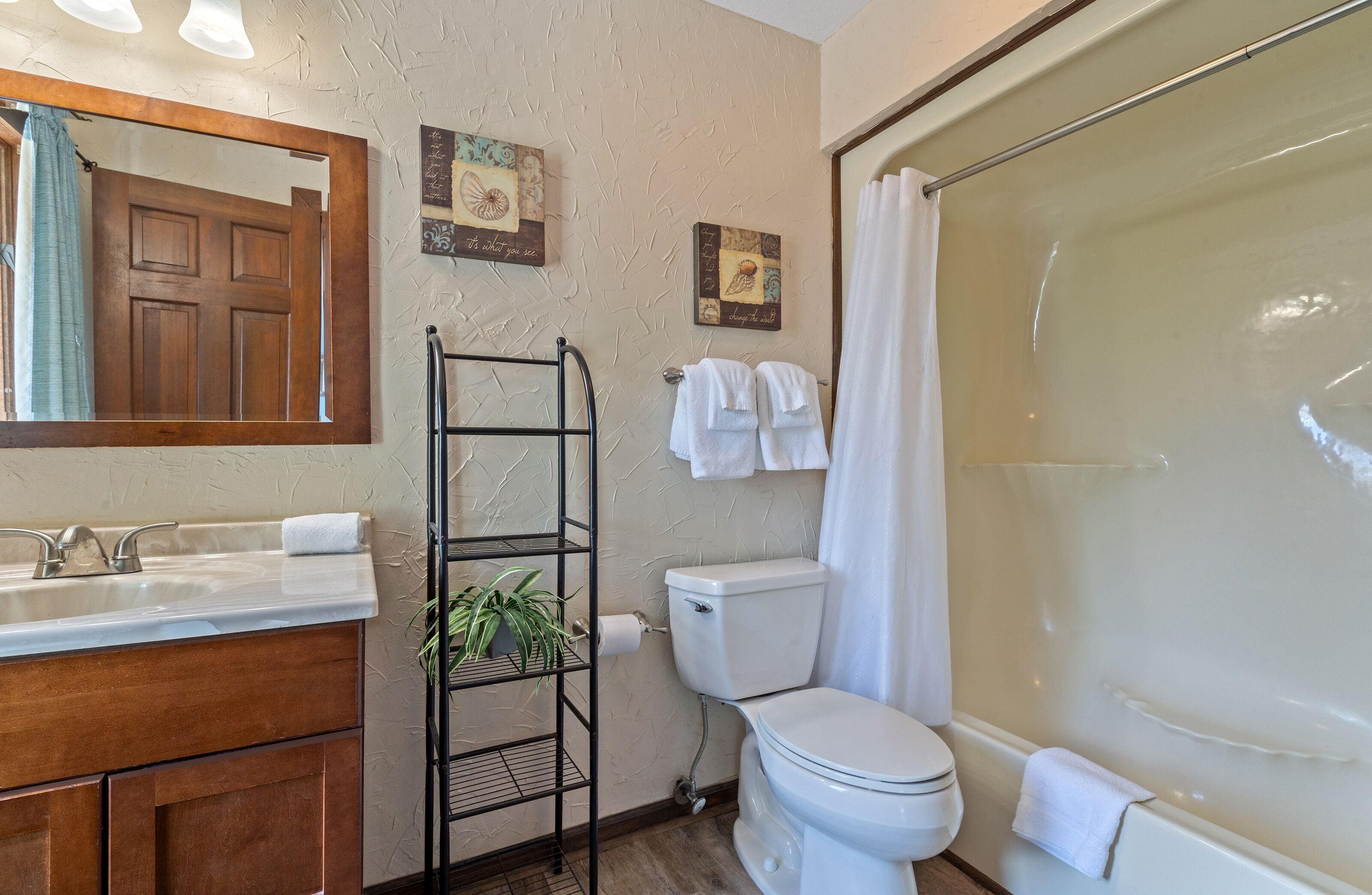 A bathroom with a wooden vanity, a toilet, a bathtub, and a shelf with a plant.