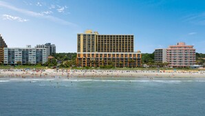 A beachfront hotel with multiple floors, a sandy beach in the foreground, and a clear blue sky. - The Caravelle Resort (Myrtle Beach)