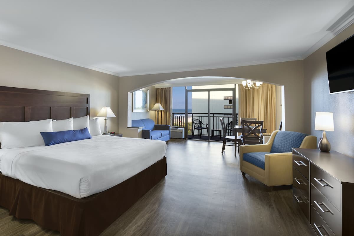 Habitación de hotel con una cama grande, un sofá, un escritorio y un balcón con sillas.