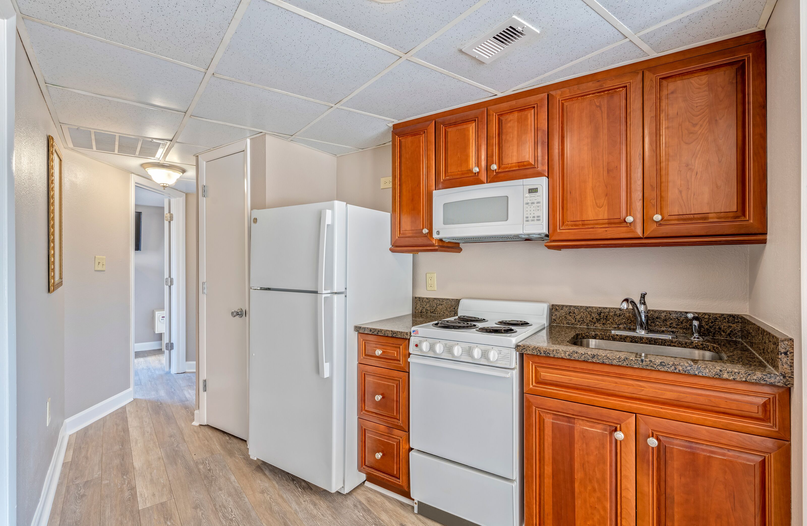 A kitchen with wooden cabinets, a white refrigerator, a microwave, a stove, and a granite countertop.
