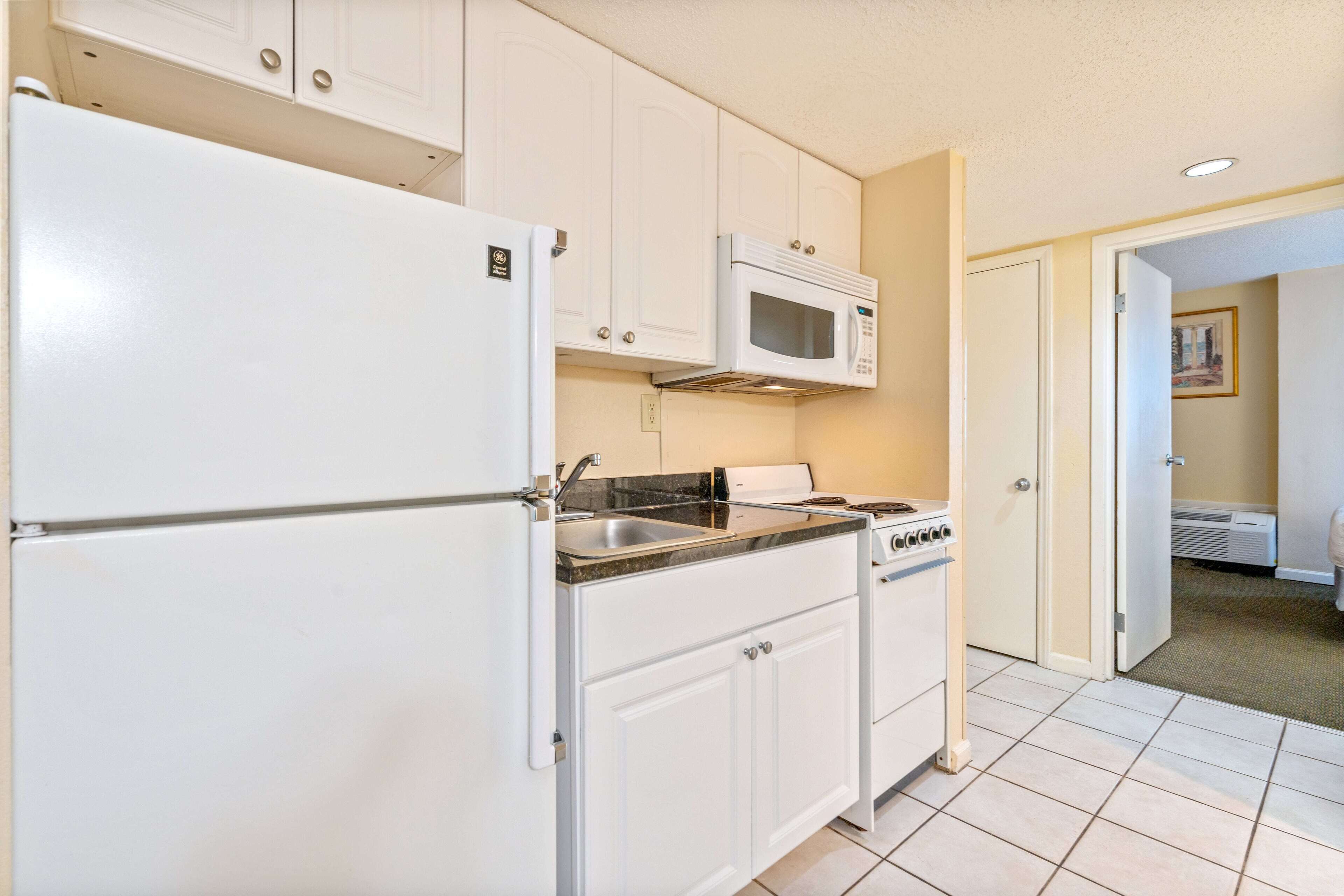 A kitchen with white cabinets, a refrigerator, a microwave, a stove, and a sink.