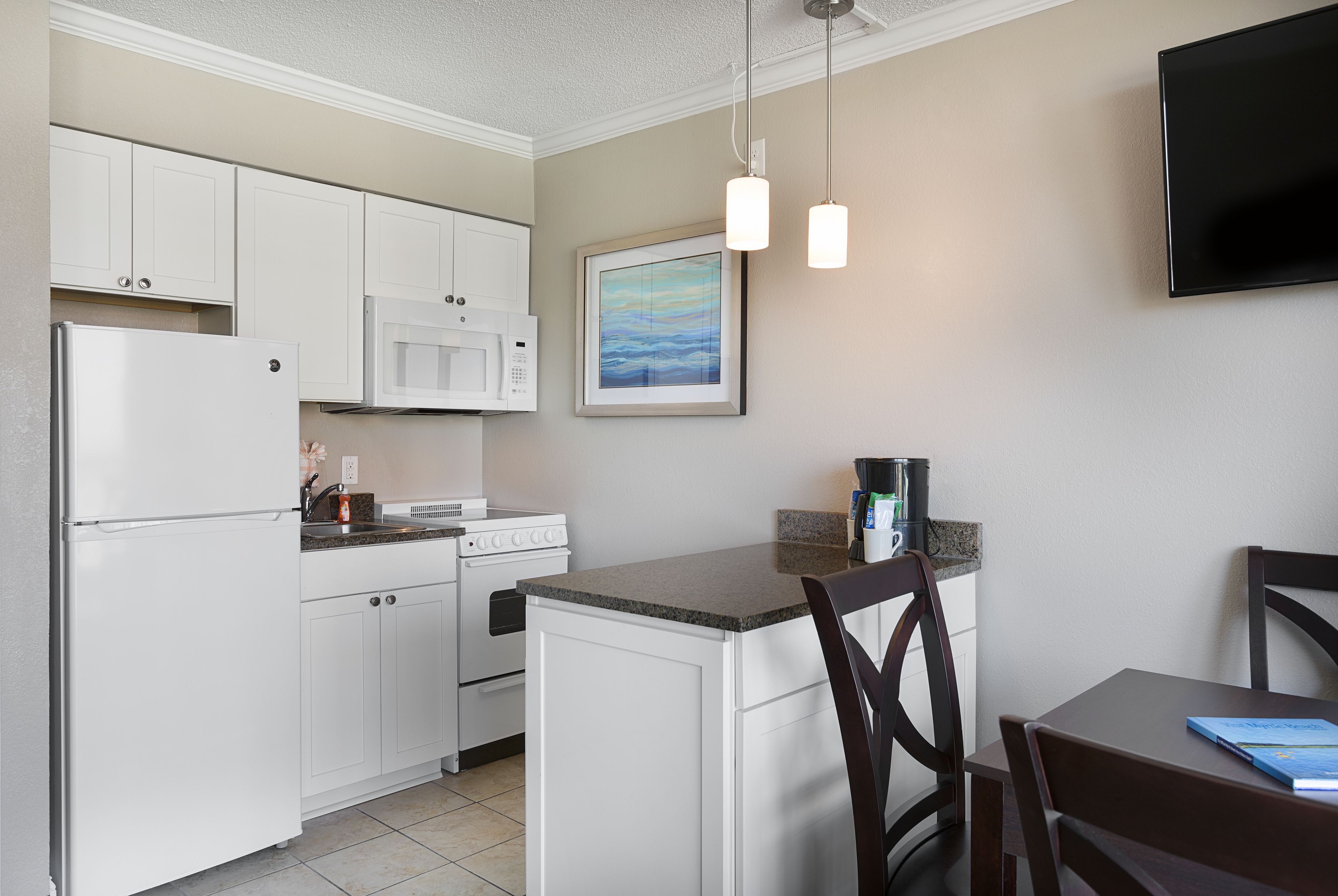 A kitchen with white cabinets, a microwave, a stove, a sink, and a dining area with a chair and a table.
