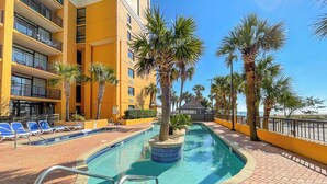A hotel pool area with a clear blue pool, sun loungers, palm trees, and a yellow building facade. - The Caravelle Resort (Myrtle Beach)