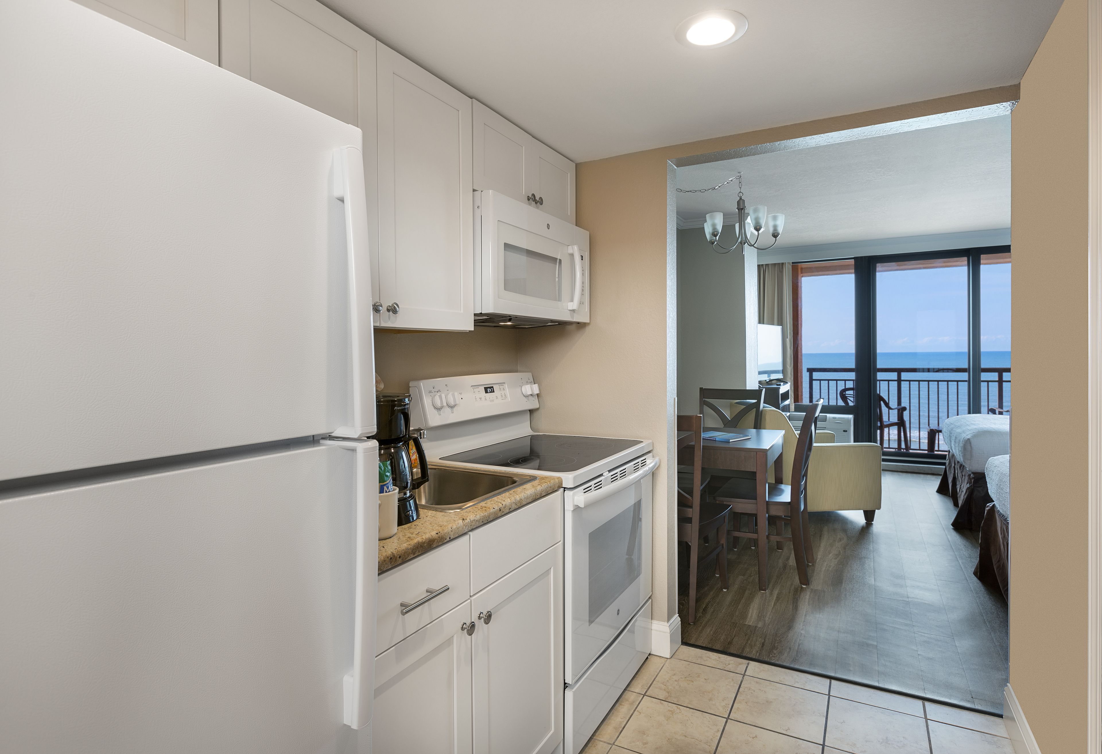 A compact kitchen with white appliances, a dining area with a table and chairs, and a balcony with a view.