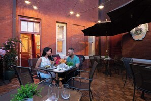 Un área de comedor al aire libre con paredes de ladrillo, sillas y mesas de metal.