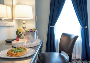 Habitación de hotel con una mesa de comedor dispuesta con una pizza, una lámpara y un florero con flores.