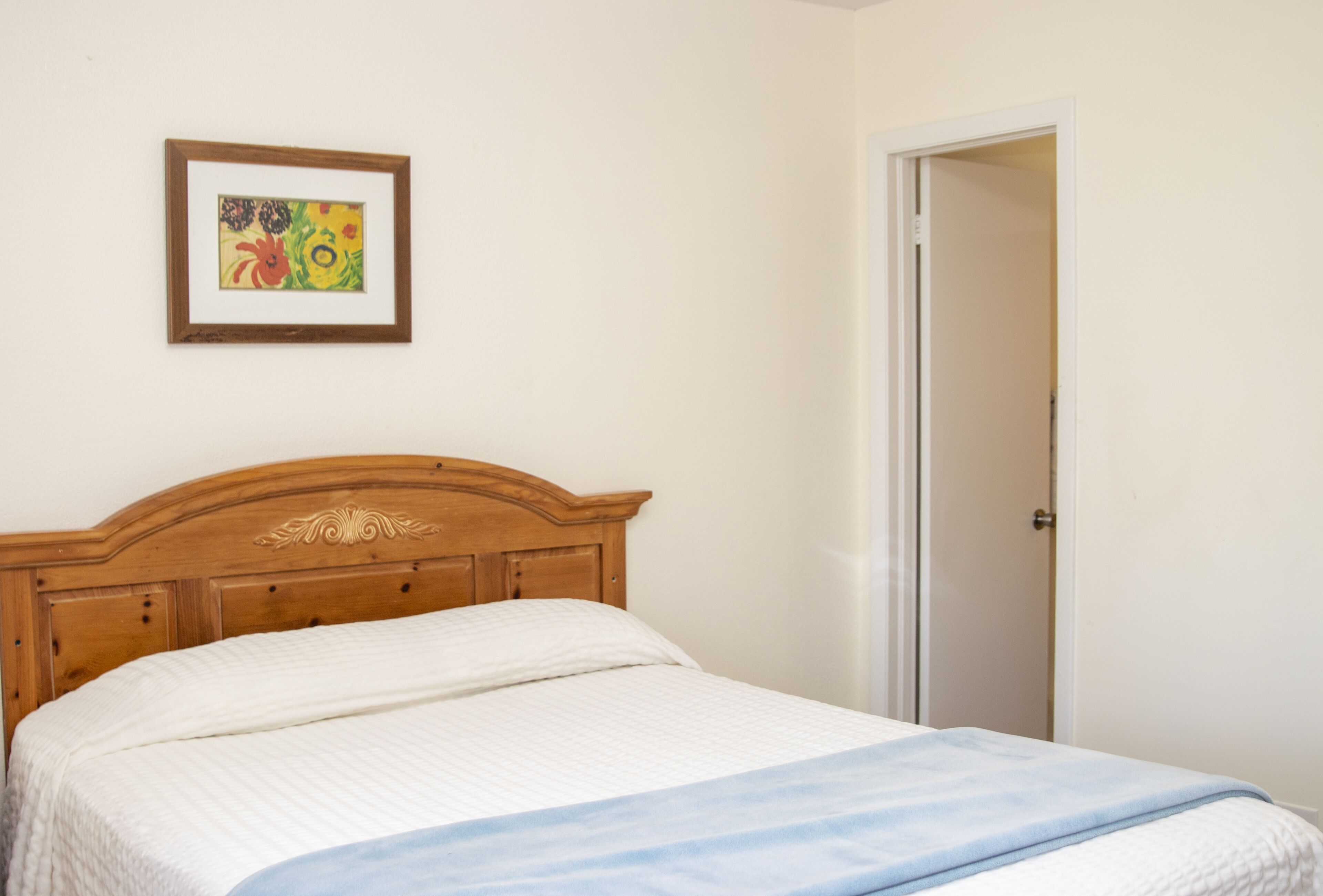 A bedroom with a wooden headboard, a bed with a white and blue blanket, and a framed picture on the wall.