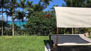 Un área verde con una estructura de toldo blanco, rodeada de palmeras y vista al océano.