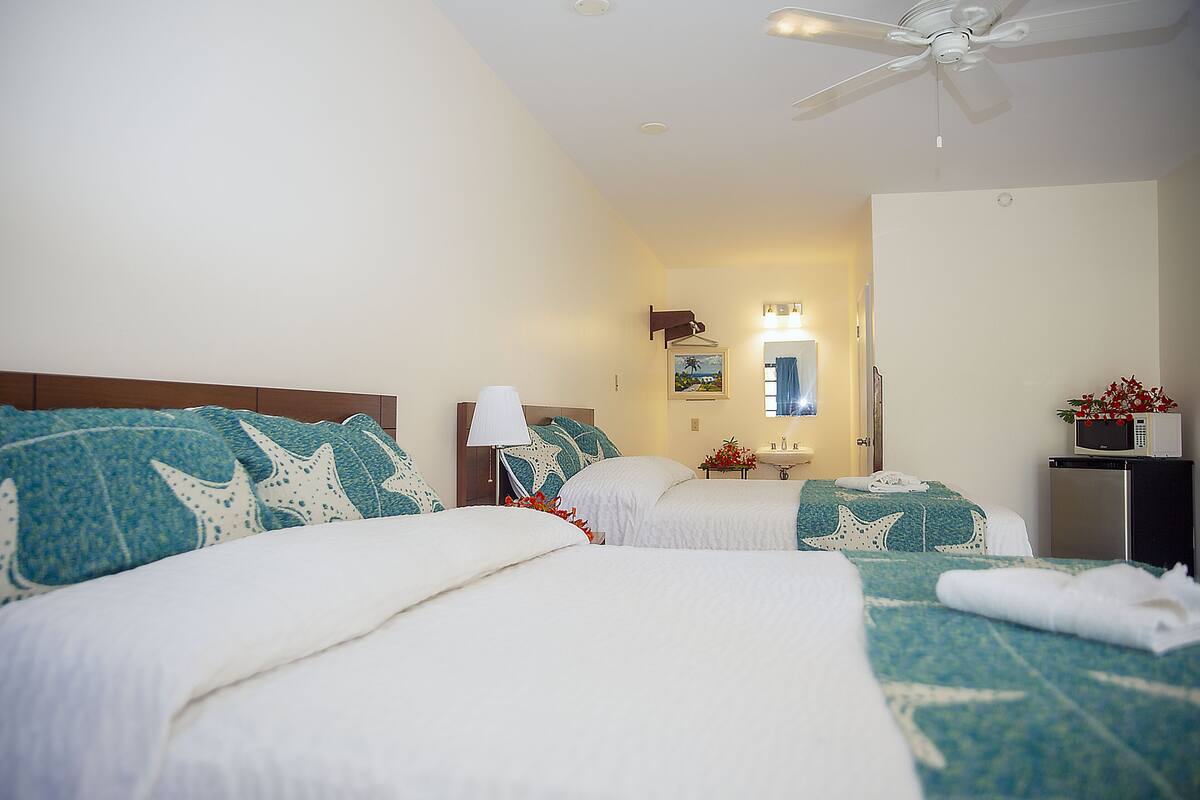 A hotel room with two beds, a ceiling fan, a TV, and a bathroom visible through an open door.