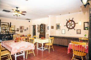 A dining area with a table set for four, surrounded by wooden chairs, a ceiling fan, and a ship's wheel decoration on the wall. - Orange Hill Beach Inn (Nassau)