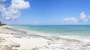 Uma praia com águas azul-turquesa cristalinas, areia branca e afloramentos rochosos.