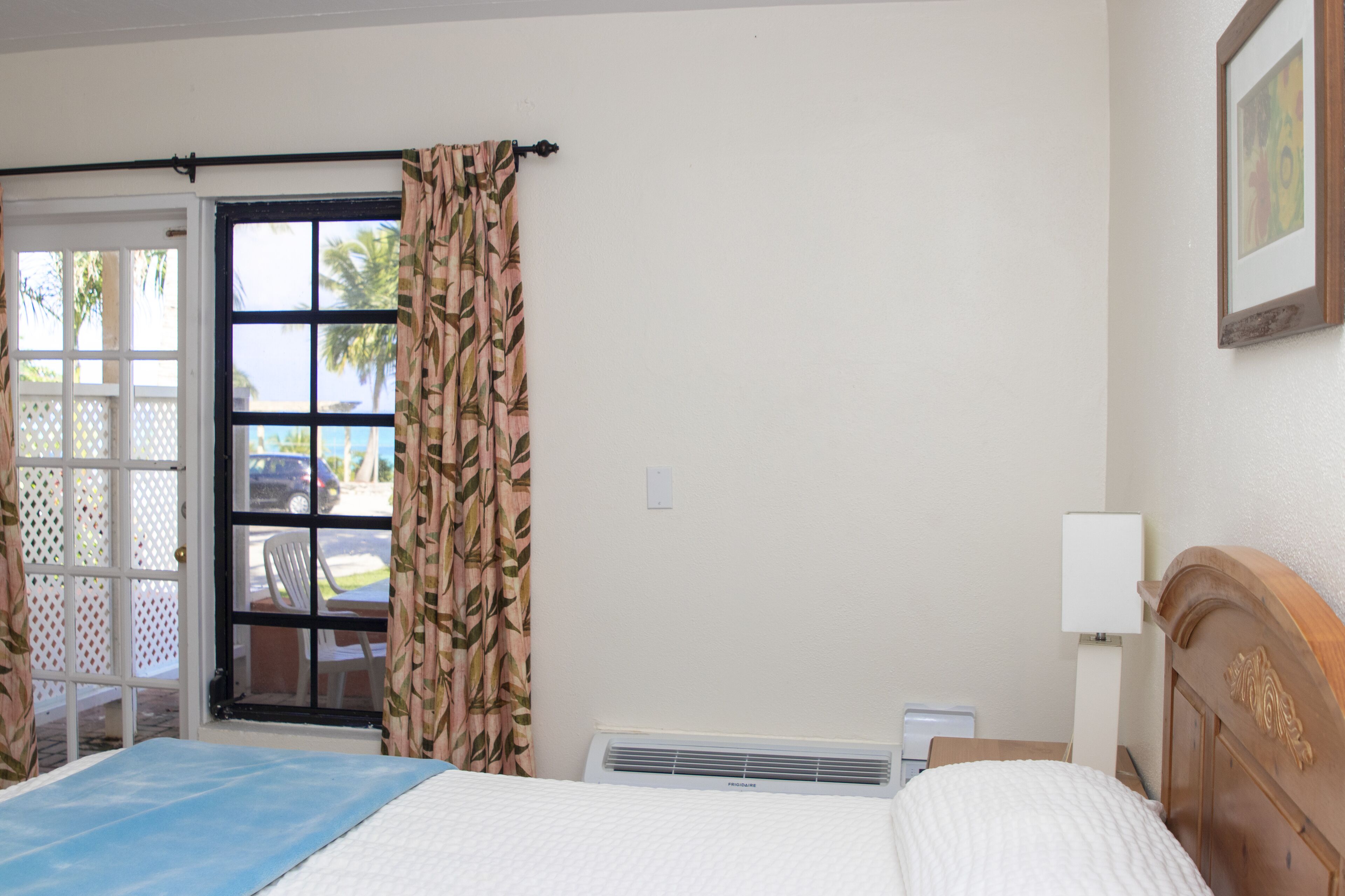Una camera d'albergo con un letto, una scrivania, una sedia, una finestra con tende, un condizionatore d'aria e una porta che dà all'esterno.