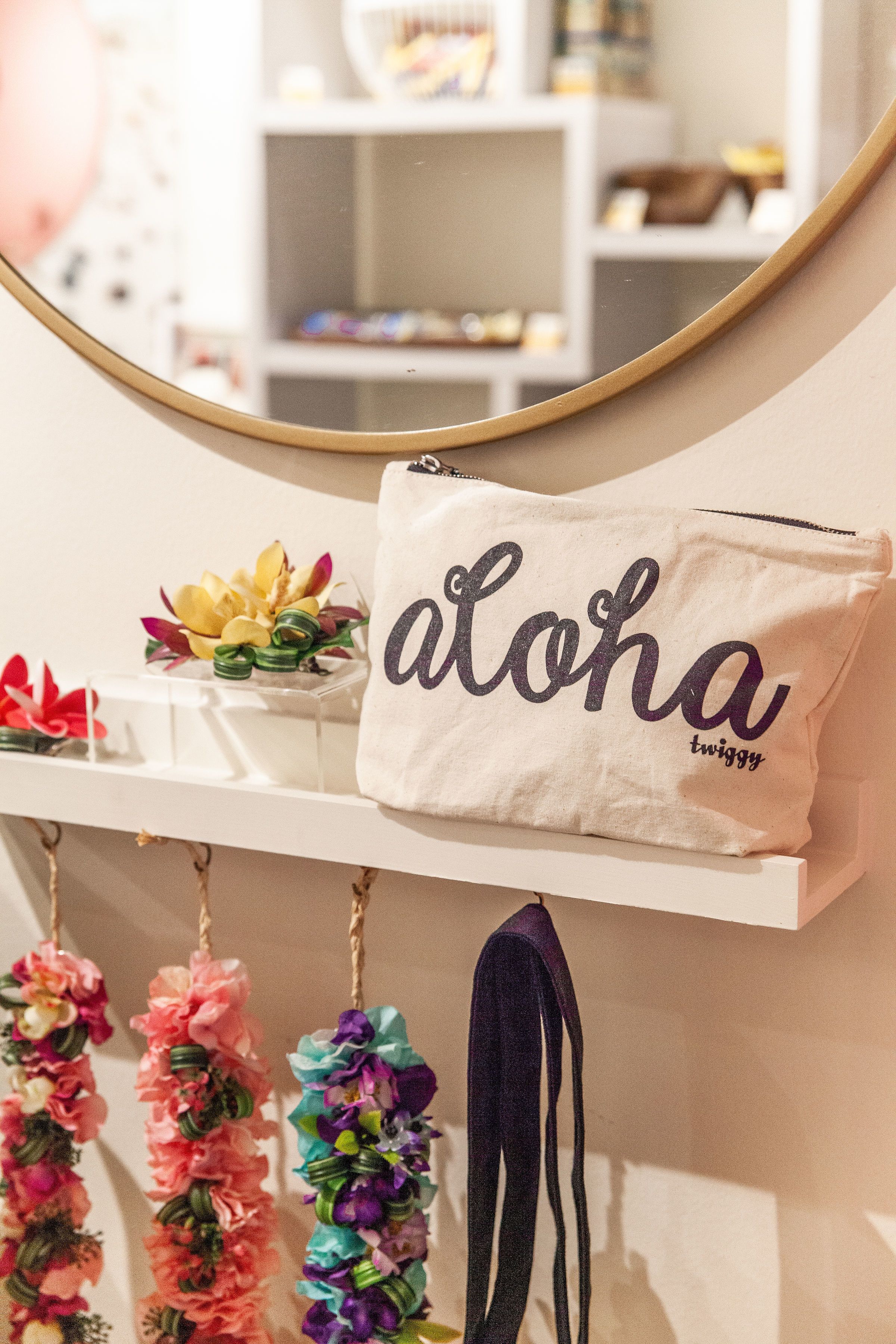 Una estantería con una bolsa blanca etiquetada "aloha twiggly" y coloridos collares de flores.