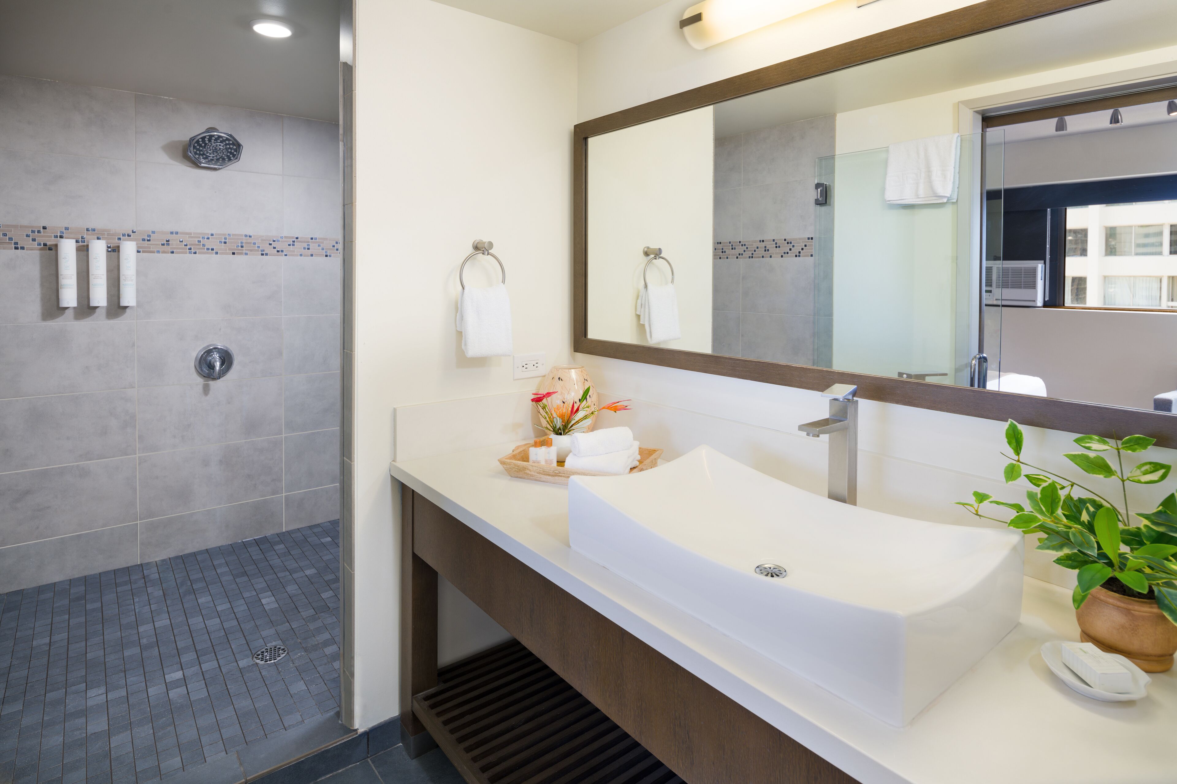 Un baño moderno con un espejo grande, un lavamanos blanco y una zona de ducha.