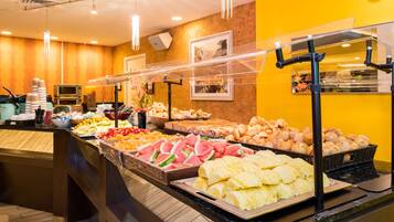 A buffet with various food items, including fruits, pastries, and sandwiches.
