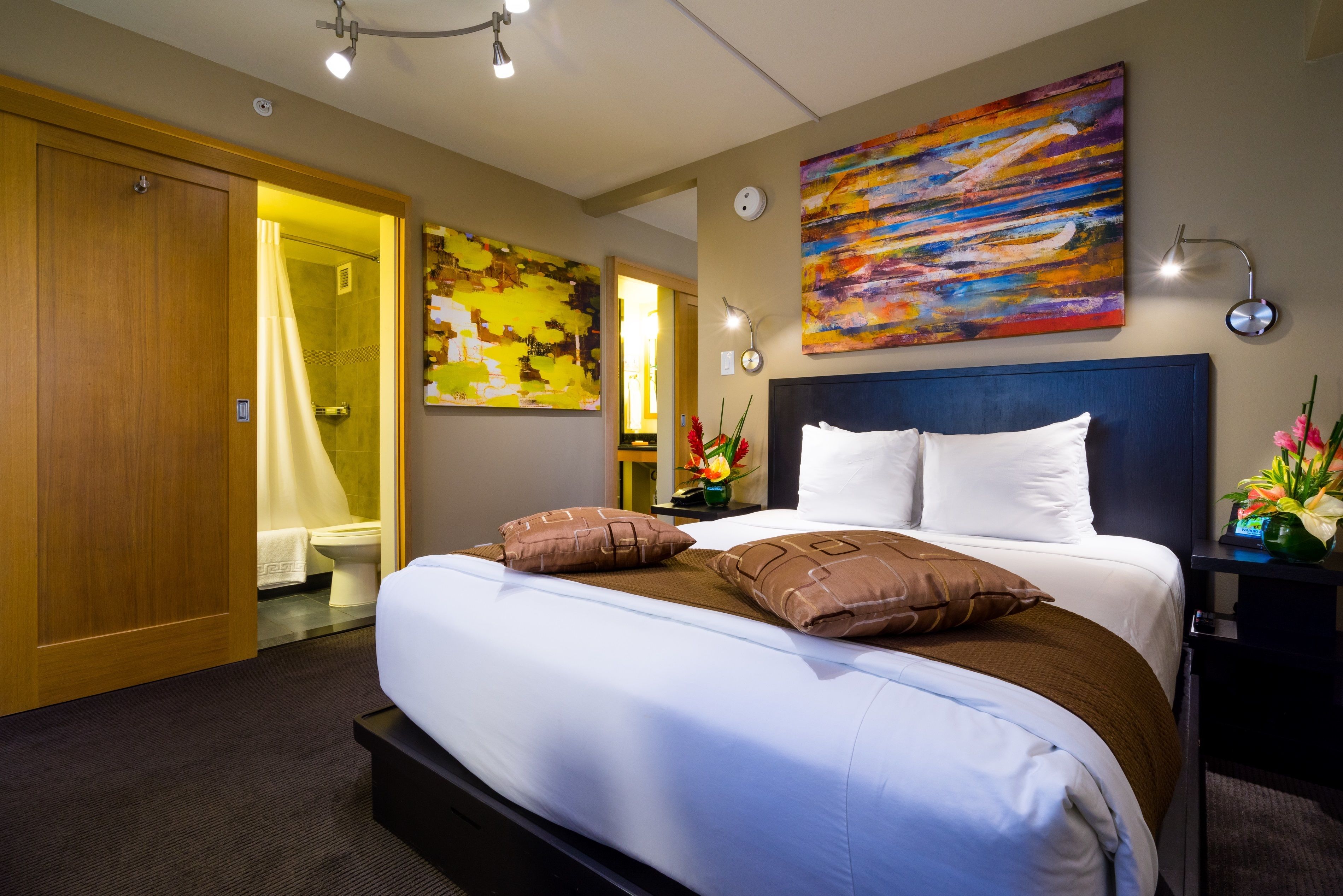 Habitación de hotel con una cama grande, un armario de madera, zona de ducha y un cuadro abstracto y colorido en la pared.