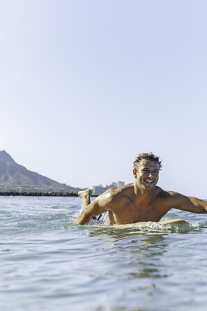 A person swimming in clear water with a mountain and buildings in the background. - Vive Hotel Waikiki (Honolulu)