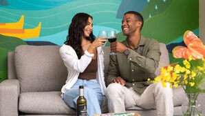 A couple sitting on a grey sofa with a glass table in front of them, holding wine glasses. - Vive Hotel Waikiki (Honolulu)