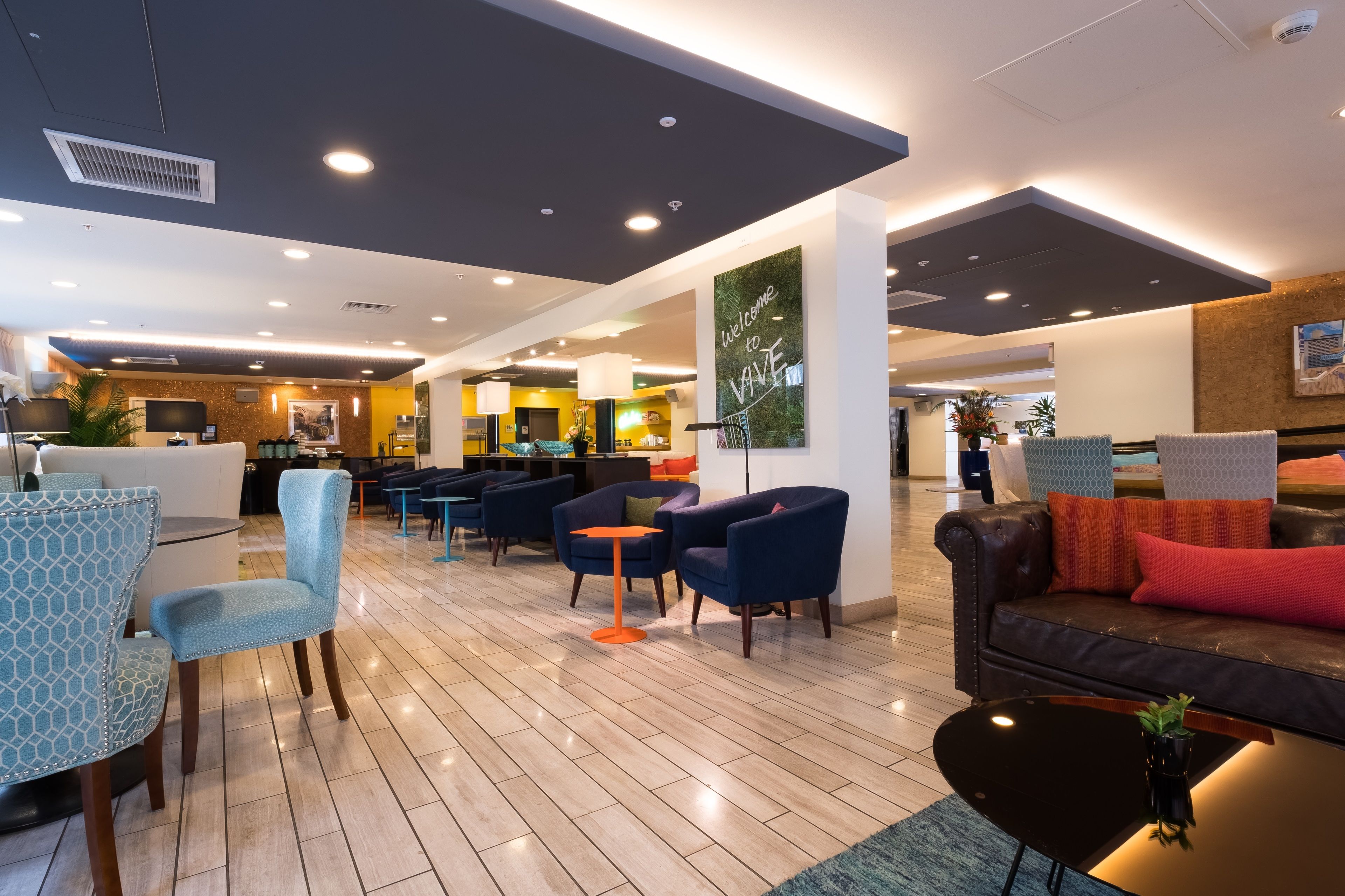 A modern lobby with seating areas, a reception desk, and a kitchen in the background.