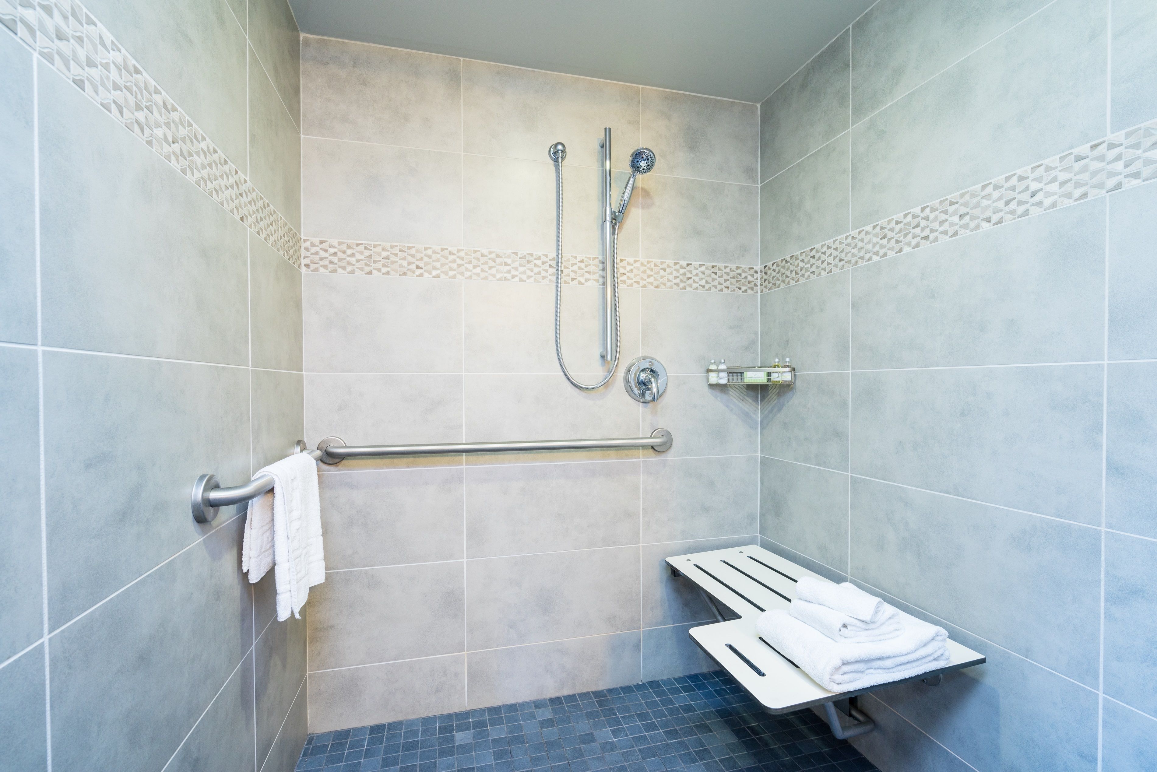 A shower area with a grab bar, a towel rack, and a shelf with folded towels.