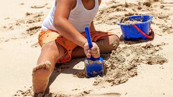 Niño jugando con arena en una playa con palmeras y edificios al fondo.