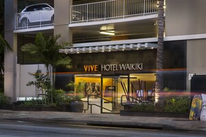 Exterior do VIVE HOTEL WAIKIKI, com design moderno e estrutura de dois andares, com um carro visível no nível superior e entrada bem iluminada.