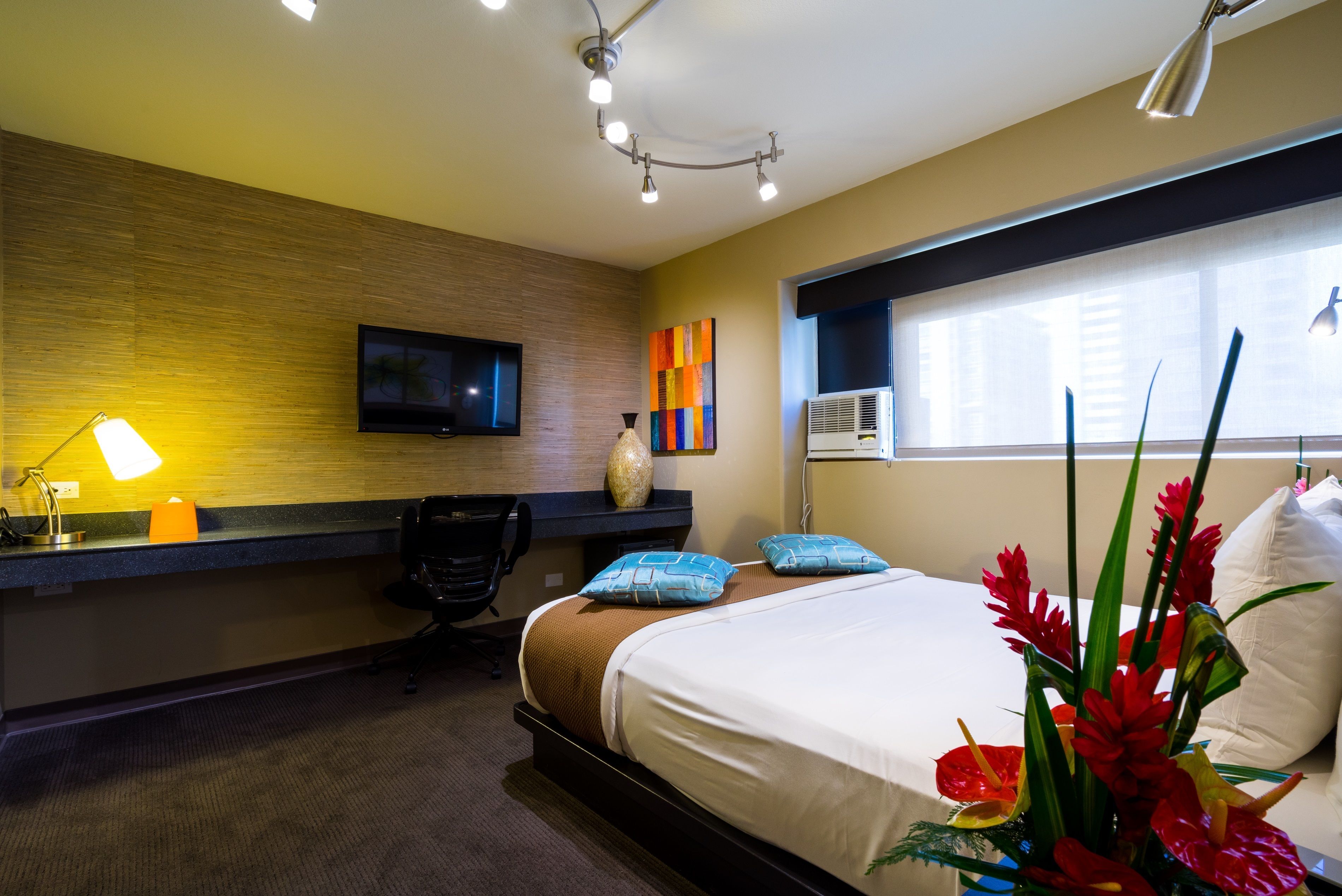 Habitación de hotel con cama, escritorio, silla, televisión y ventana con persianas.