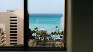 A view of a beach with a sailboat, palm trees, and a building with balconies. - Vive Hotel Waikiki (Honolulu)