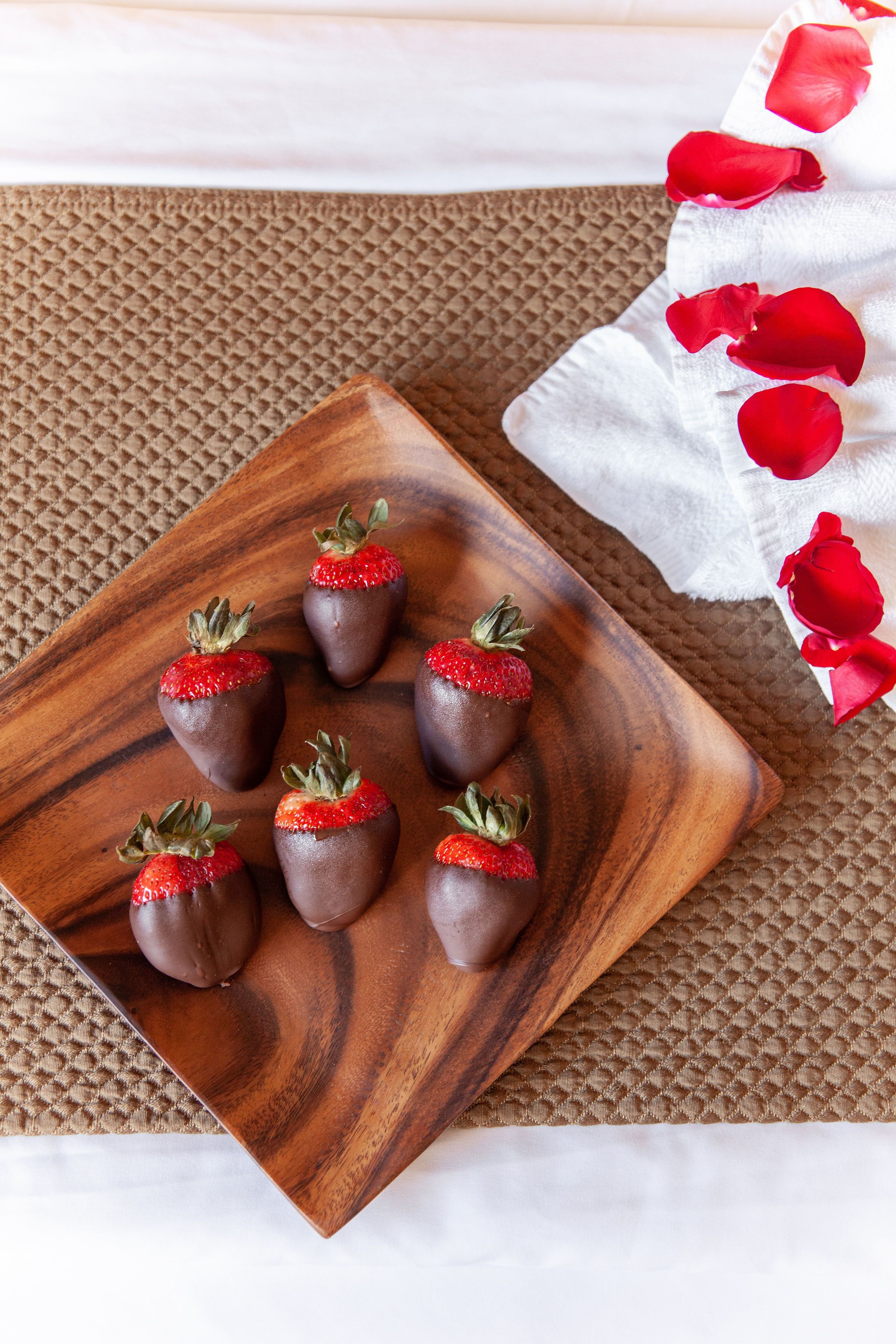 A wooden tray with chocolate-covered strawberries on a textured brown mat.