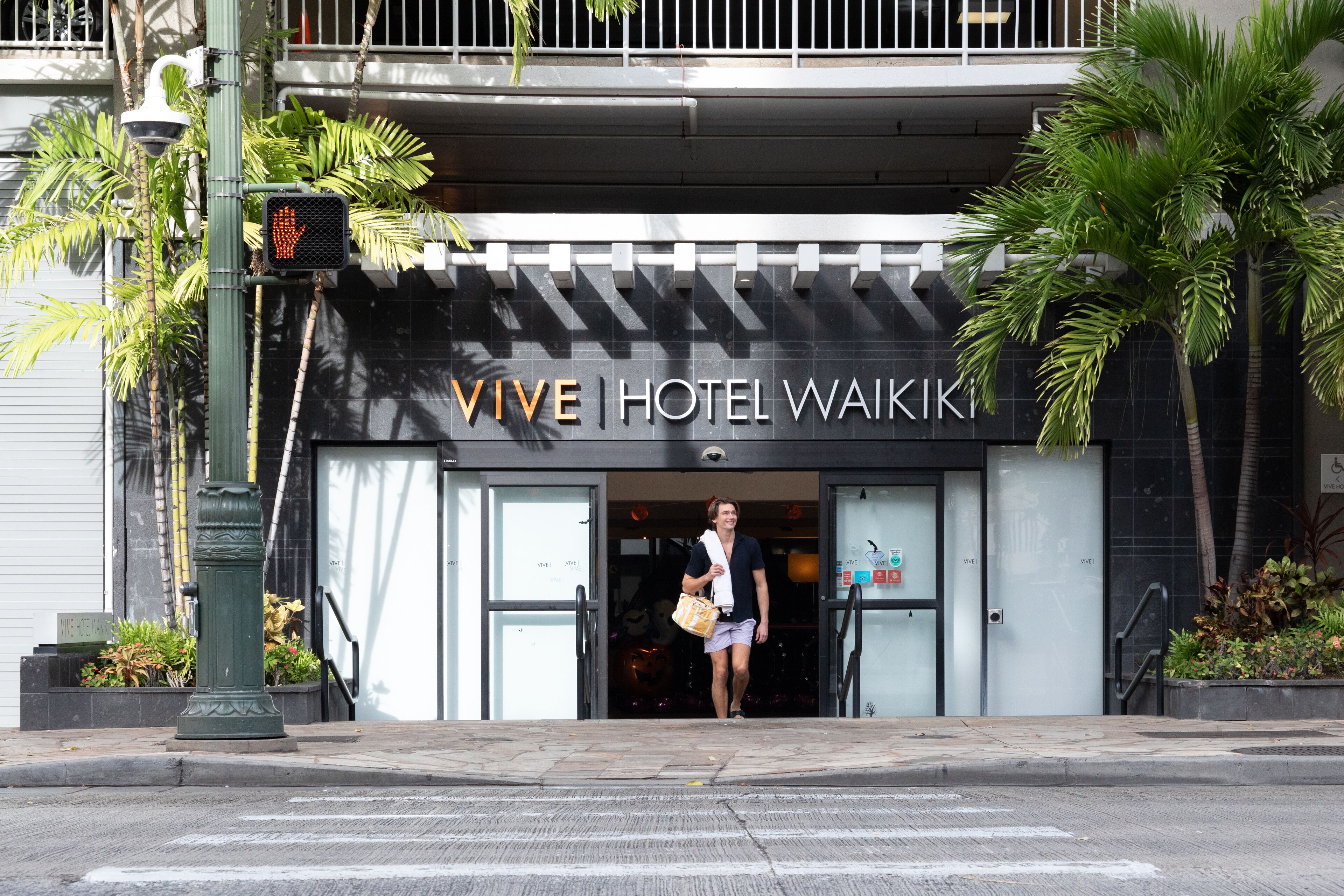 The entrance to VIVE Hotel Waikiki with a palm tree and a pedestrian crossing signal.