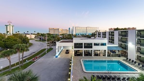 Un hotel moderno con piscina, zona de estacionamiento y vistas de edificios circundantes.