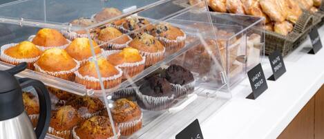 Vitrina de panadería con varios muffins y pasteles, incluyendo pan blanco y de trigo.
