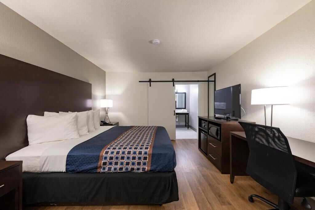 A hotel room with a bed, desk, chair, TV, and a small kitchenette.
