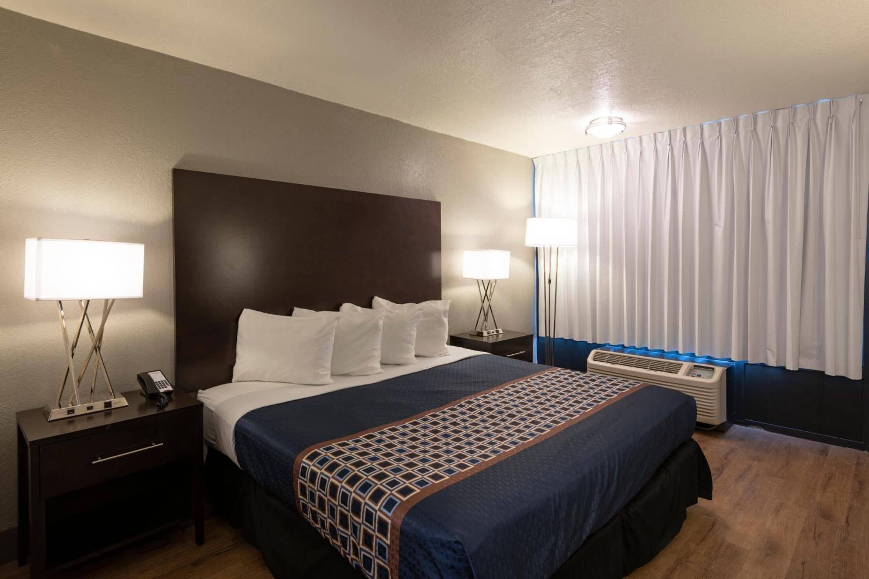 A hotel room with a large bed, two bedside tables with lamps, a heater, and a window with curtains.