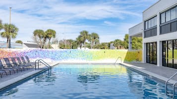 Una piscina con sillas de descanso y una pared de mosaicos coloridos.