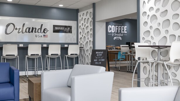 Un moderno vestíbulo de hotel con áreas de descanso, una estación de café y un bufé de desayuno.