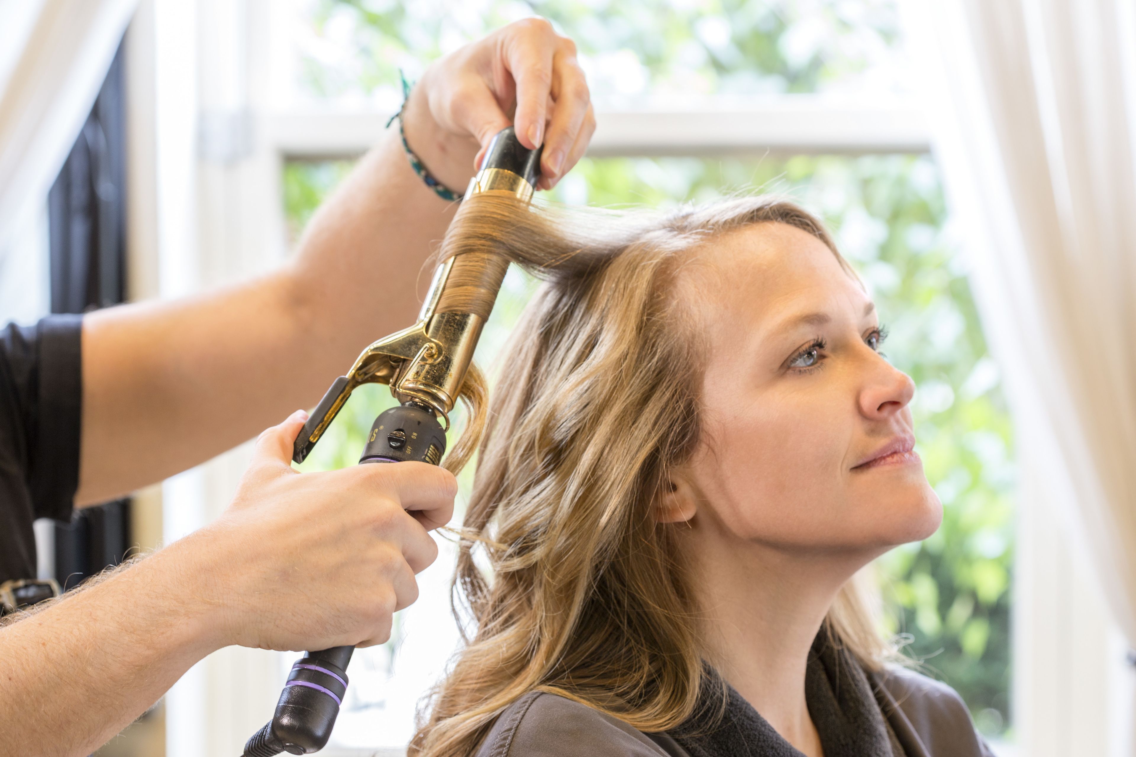 A person styling another person's hair with a curling iron.
